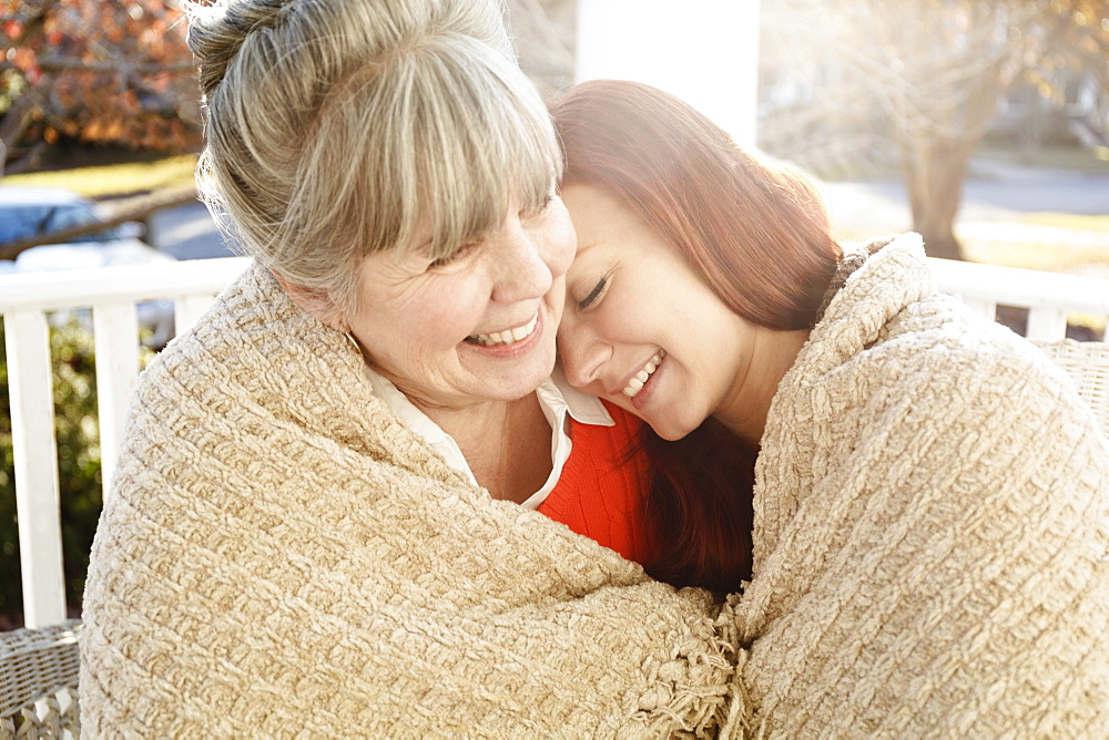 Senior woman and adult daughter wrapped in a blanket on porch