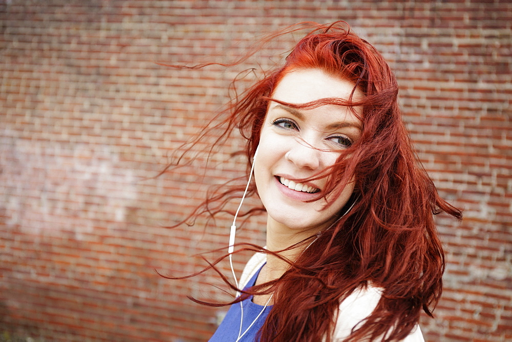 Young woman with long red hair, wearing earphones, close-up