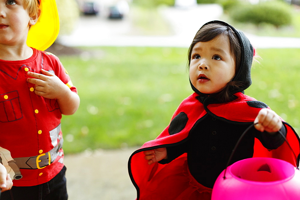 Girl and boy wearing fancy dress costumes with trick or treat bucket