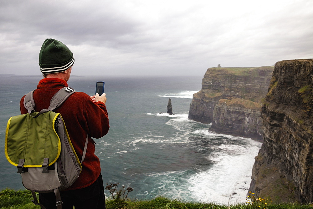 Mid adult man taking photo, Cliffs of Moher, The Burren, County Clare, Ireland