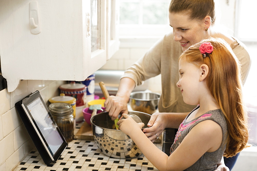 Girl and mother looking at recipe on digital tablet in kitchen