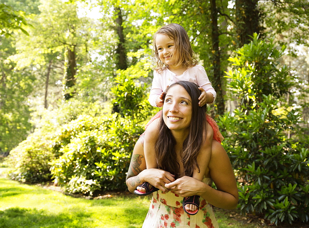 Mother giving toddler daughter a shoulder carry in park