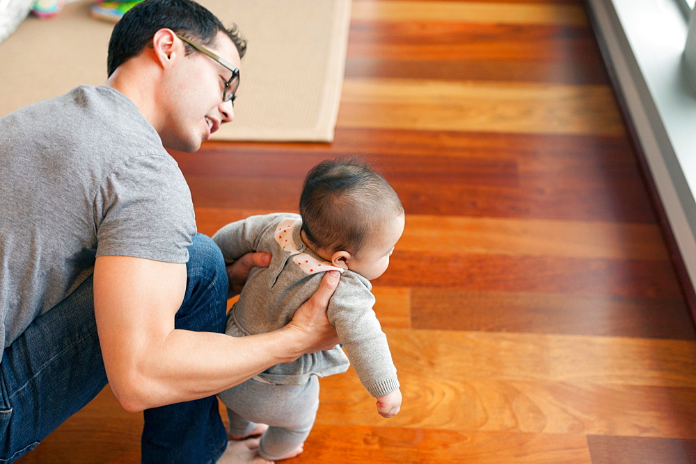 Father supporting baby girl to walk