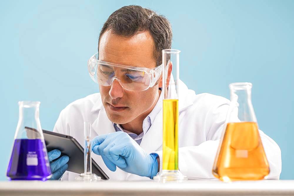 Scientist with digital tablet looking at yellow liquid in measuring beaker