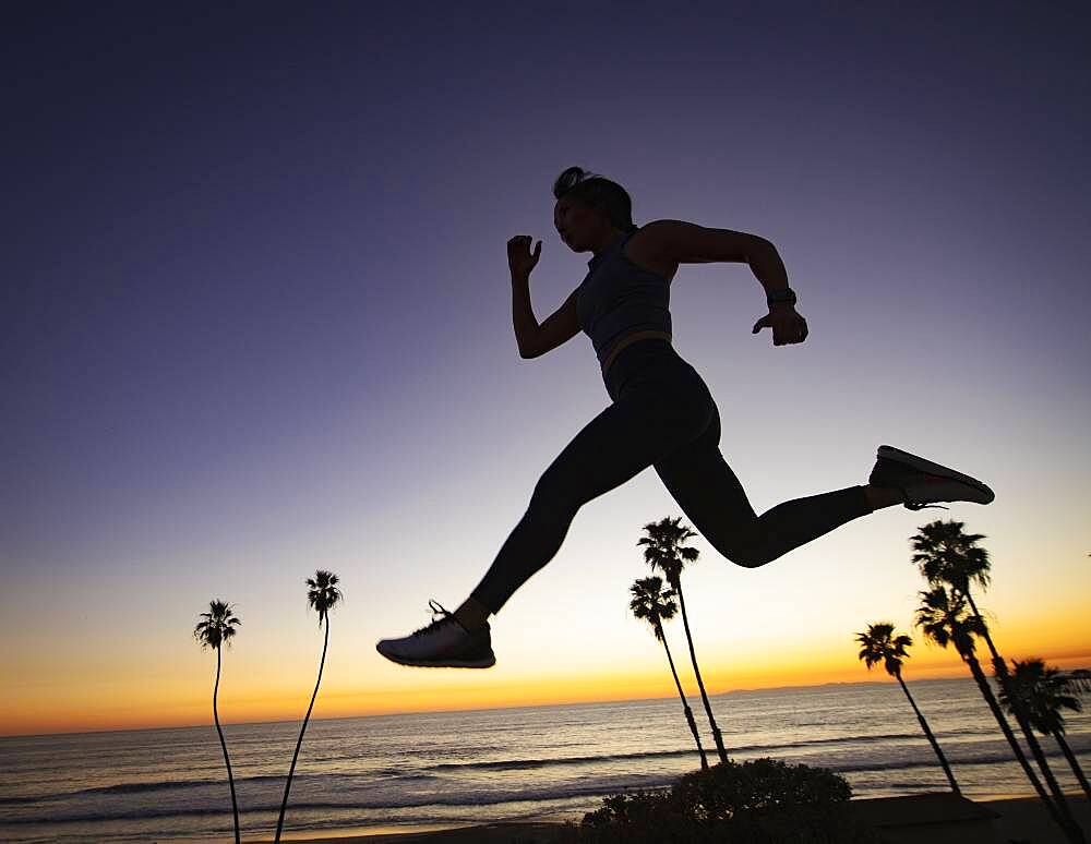 Silhouette of woman jumping on beach at sunset