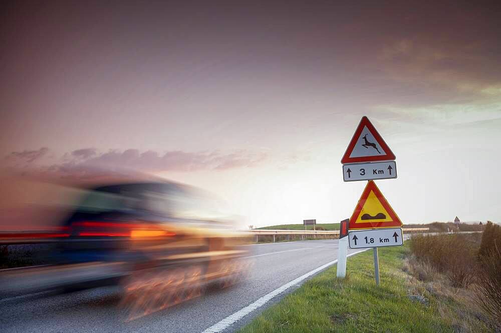 Italy, Tuscany, Val D'Orcia, Car on country road at sunset, blurred in motion