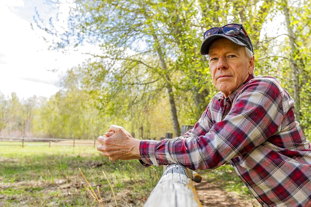 Portrait of senior farmer leaning on wooden fence near Sun Valley