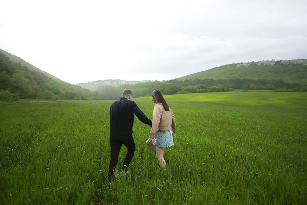 Rear view of young couple walking in wheat field in rain