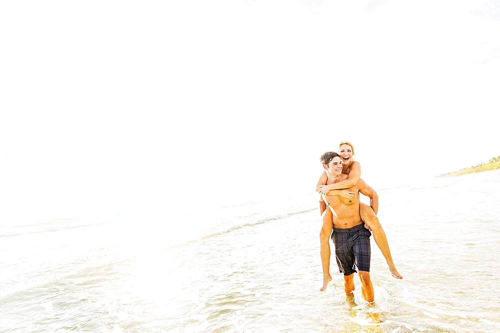 Boyfriend walking in surf carrying girlfriend piggyback, Jupiter, Florida