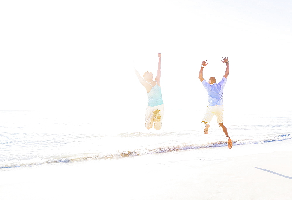 Mature couple jumping in sea with arms raised