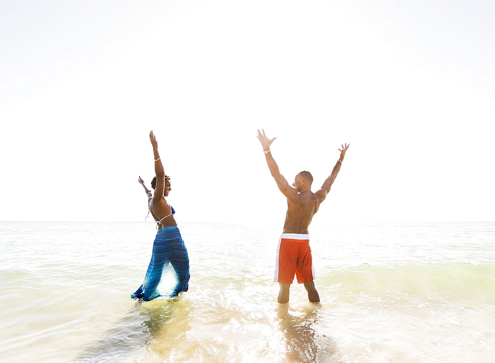Mature couple standing in sea with arms raised