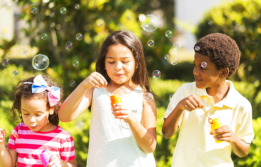 Girls( 4-5, 8-9) and boy (6-7) blowing soap bubble