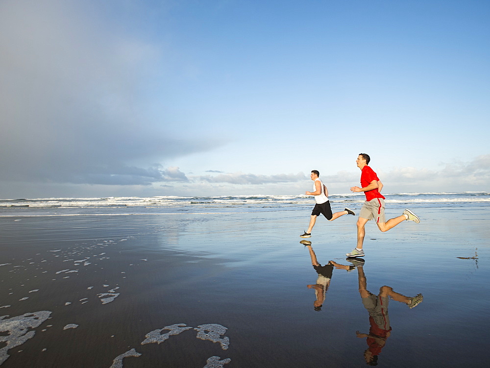 Young adult men running on beach, Rockaway Beach, Oregon