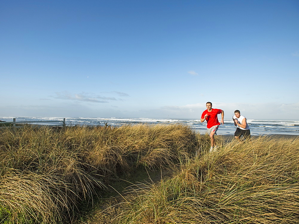 Young adult men running on dune, Rockaway Beach, Oregon