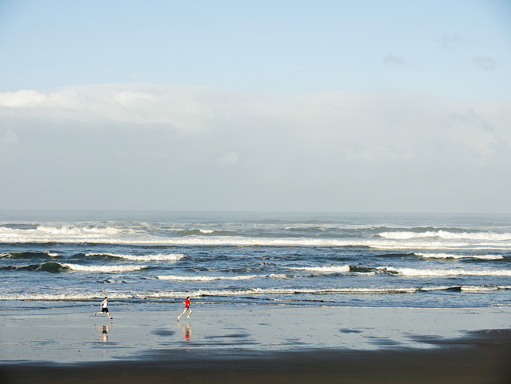 Young adult men running on beach, Rockaway Beach, Oregon