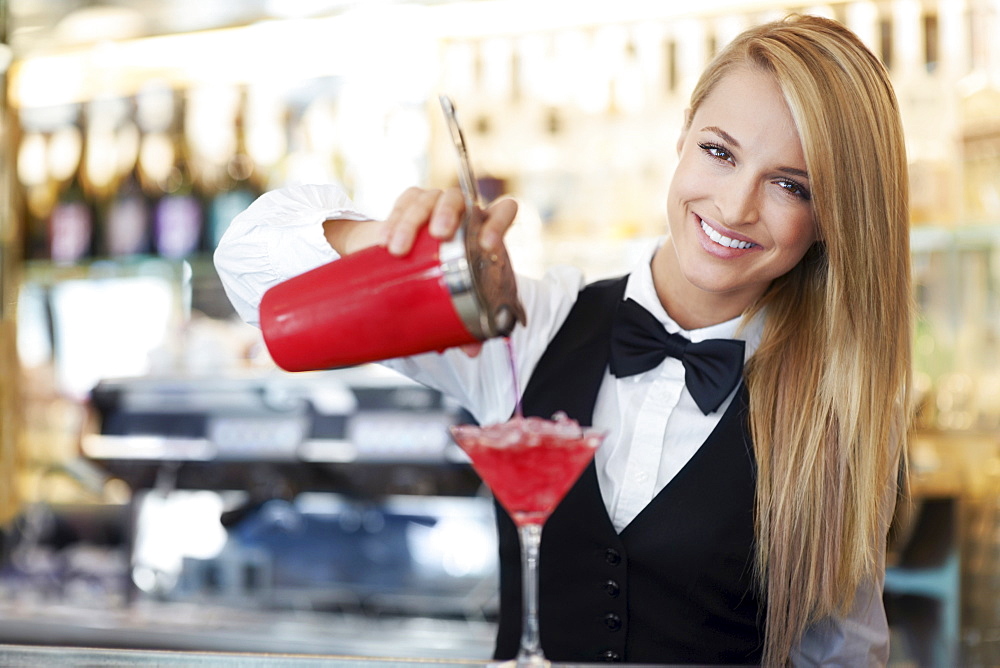 Young female bartender pouring cocktail 