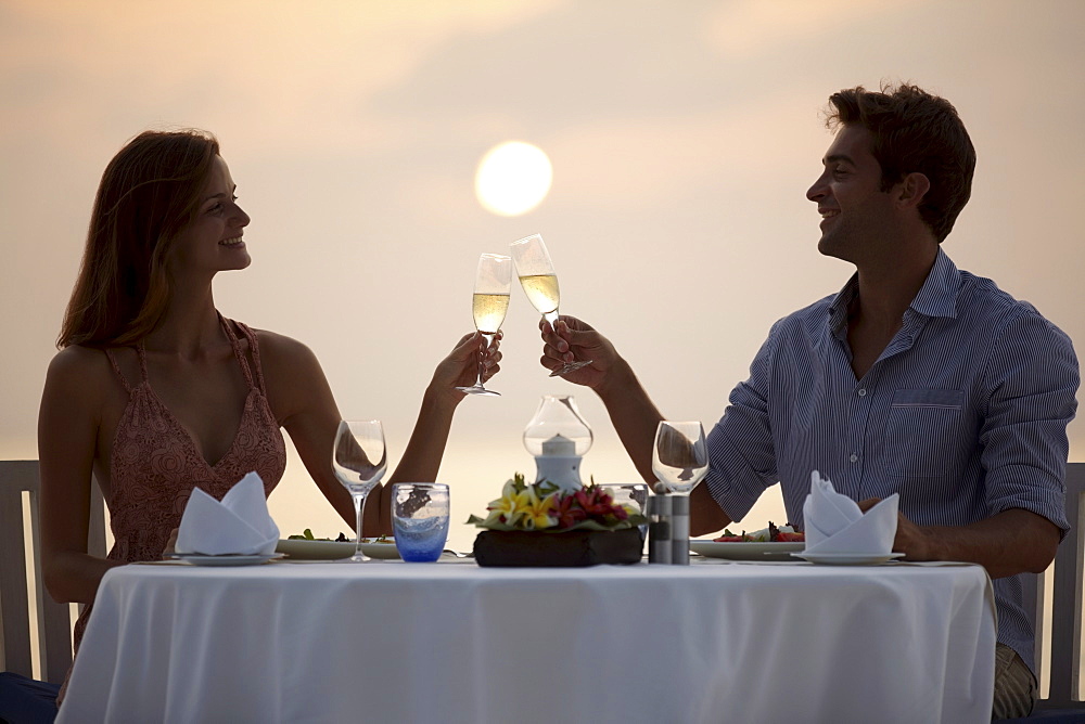 Couple at table on beach, toasting, Thailand 