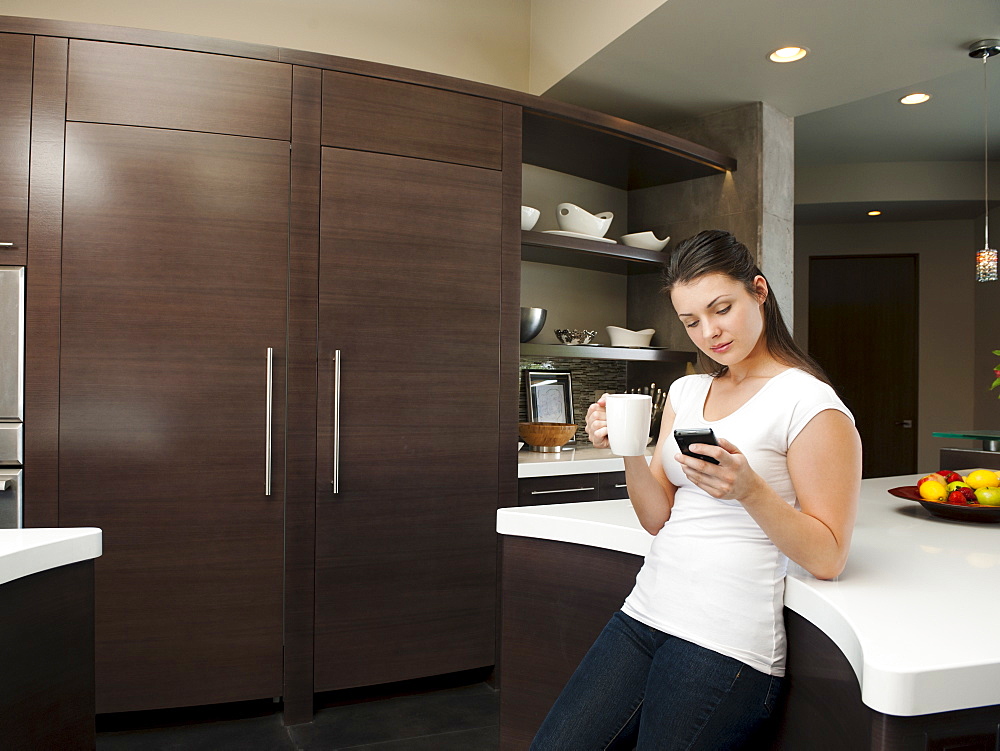 Young attractive woman enjoying morning cup of coffee while checking messages on her mobile phone