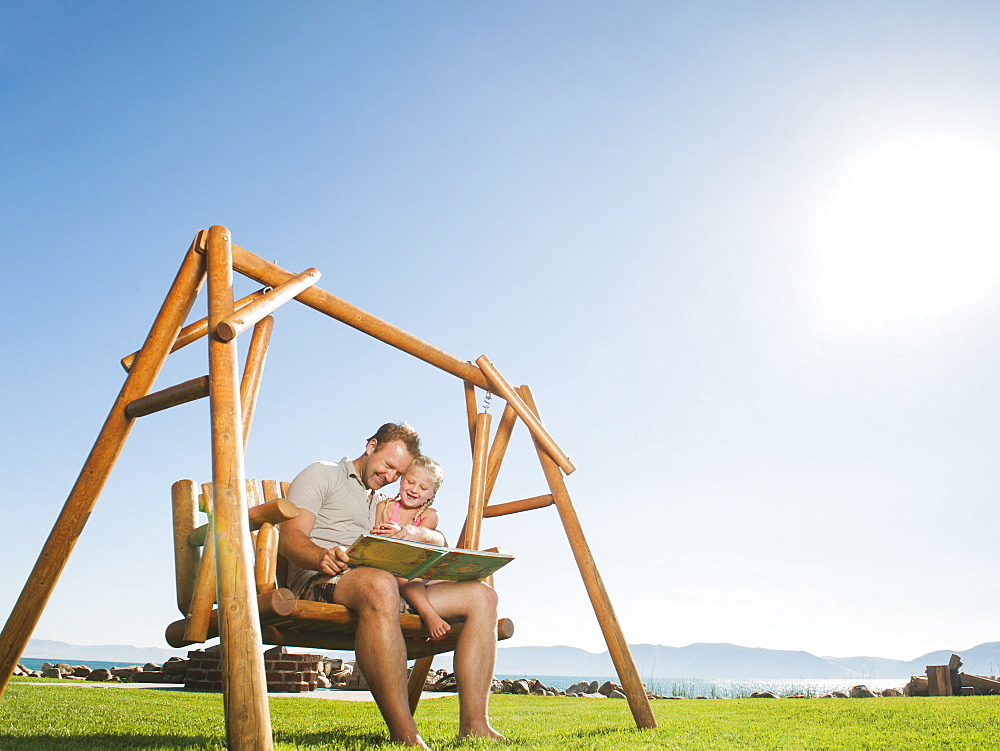 Father with daughter (4-5) on swing reading book, USA, Utah, Garden City