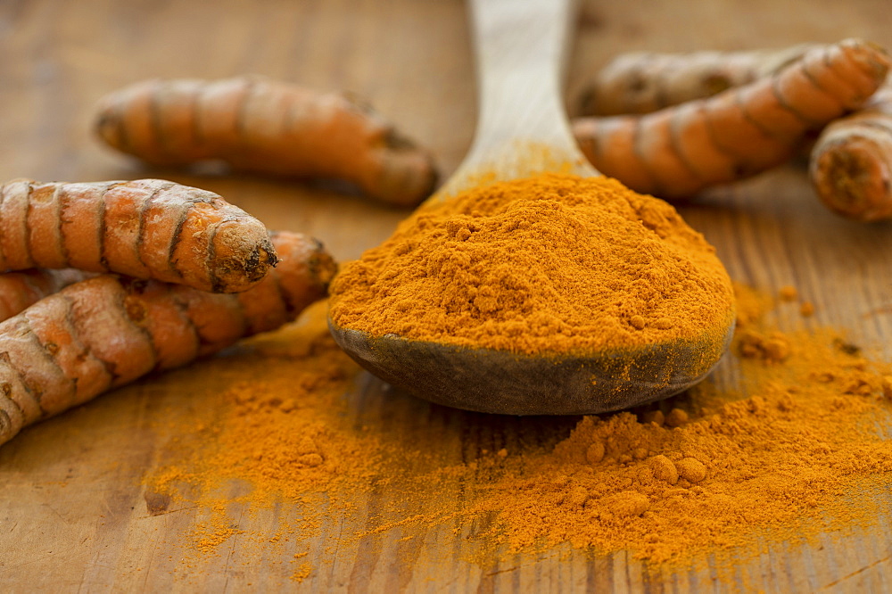 Turmeric powder and root on wooden surface