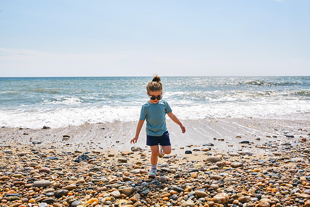 Girl (2-3) wearing sunglasses walking on pebbled beach