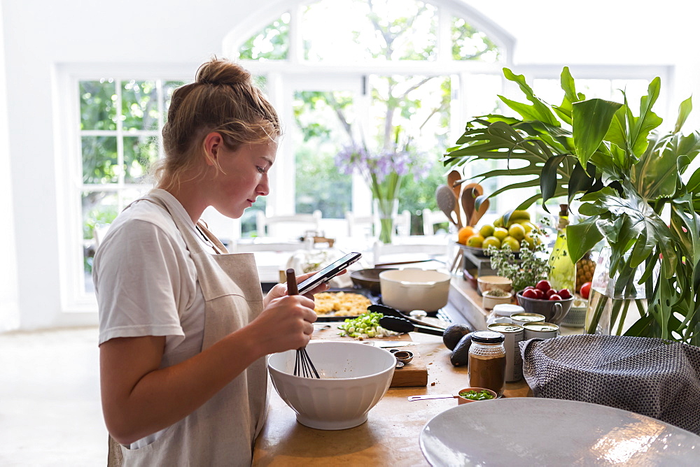 Girl (16-17) using phone while preparing meal in kitchen