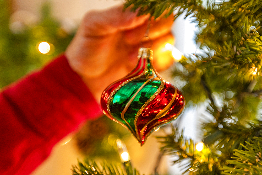 Hand hanging glass Christmas ornament on Christmas tree