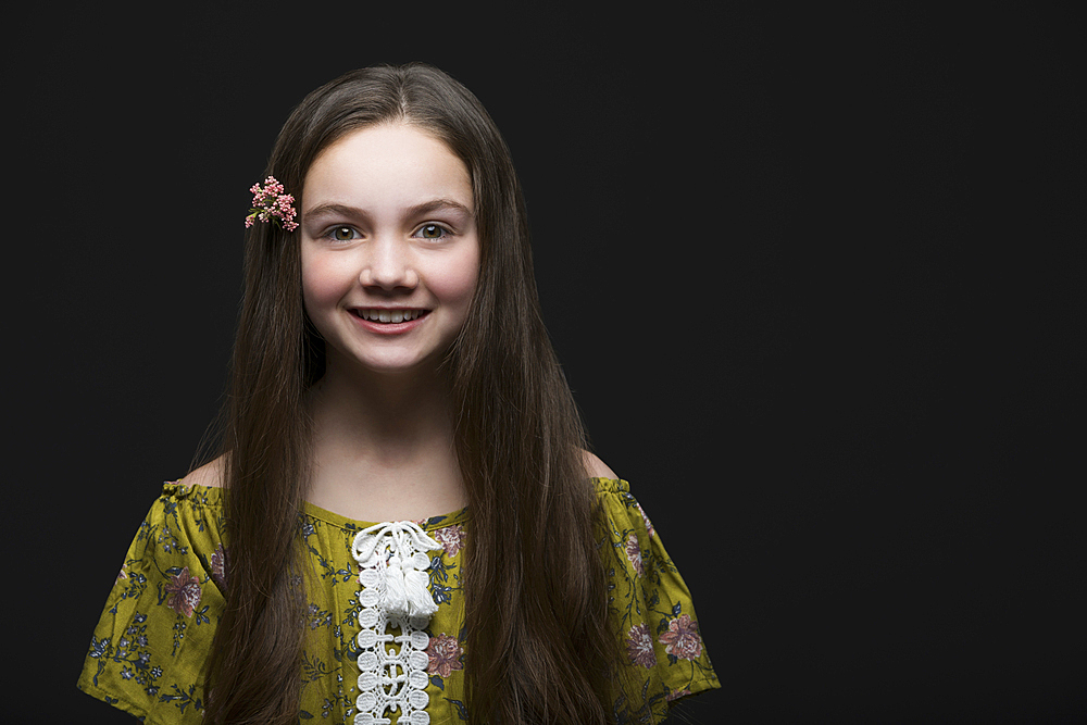 Studio portrait of smiling girl (10-11) in green dress with flower in hair