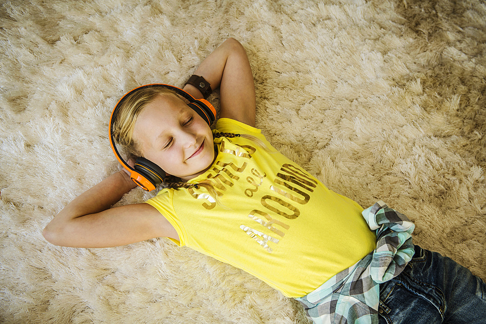 Smiling girl (10-11) with headphones lying on hairy rug with eyes closed