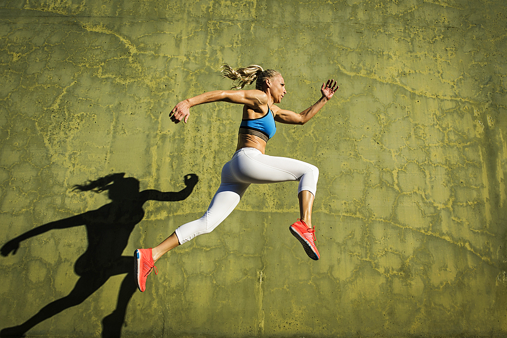Athlete woman jumping against wall