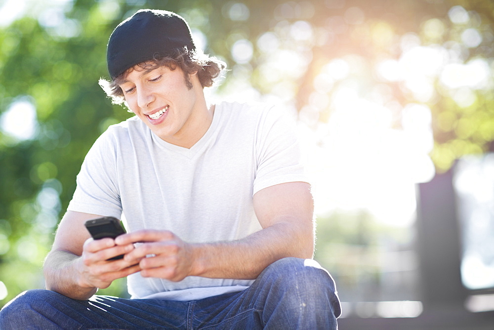 Young man sitting outdoors, text messaging