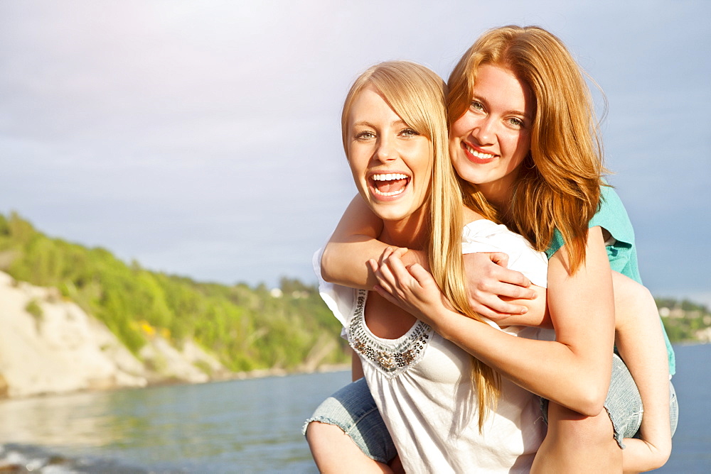 Portrait of two young women piggy-backing on beach