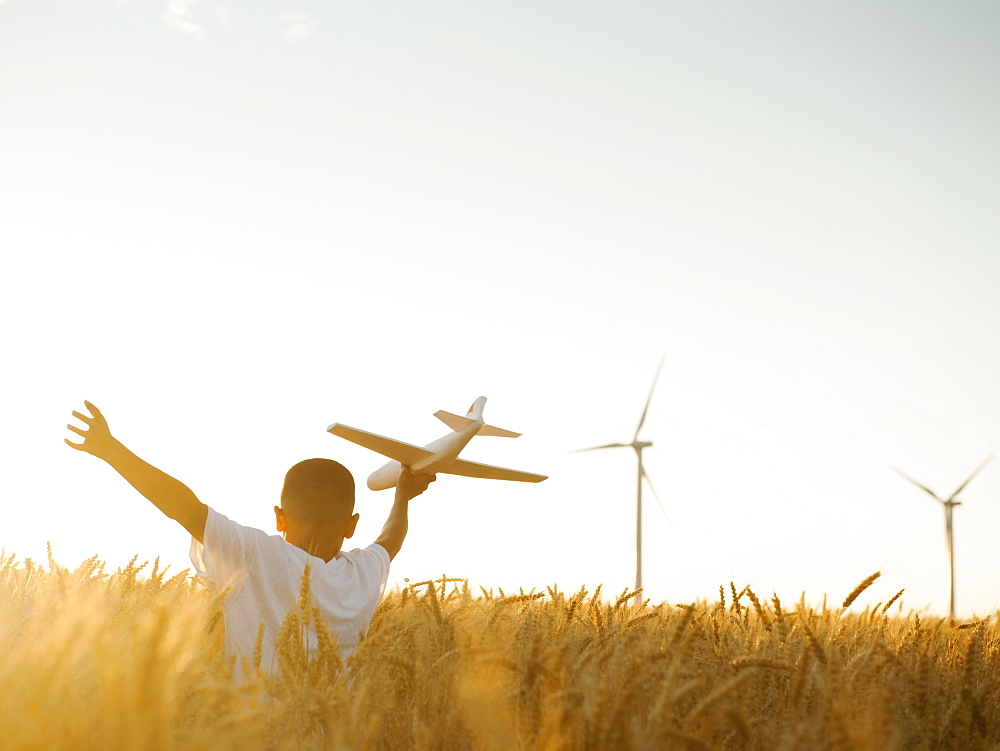 Boy (10-11) playing with toy aeroplane in wheat field