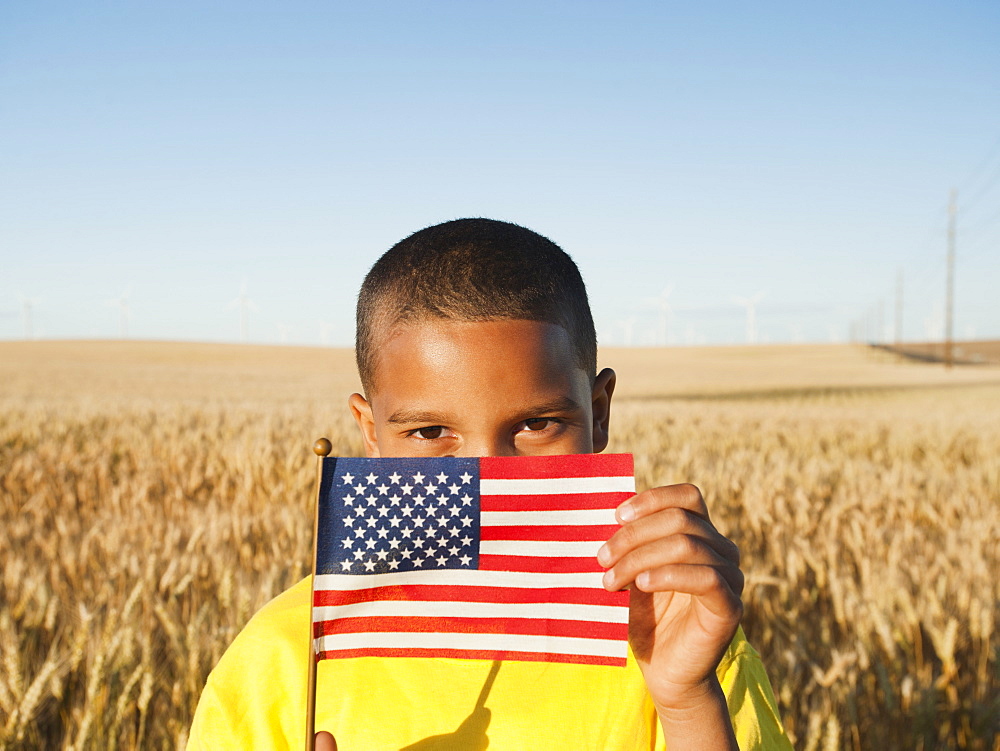 Boy (8-9) holding a small American flag in wheat field