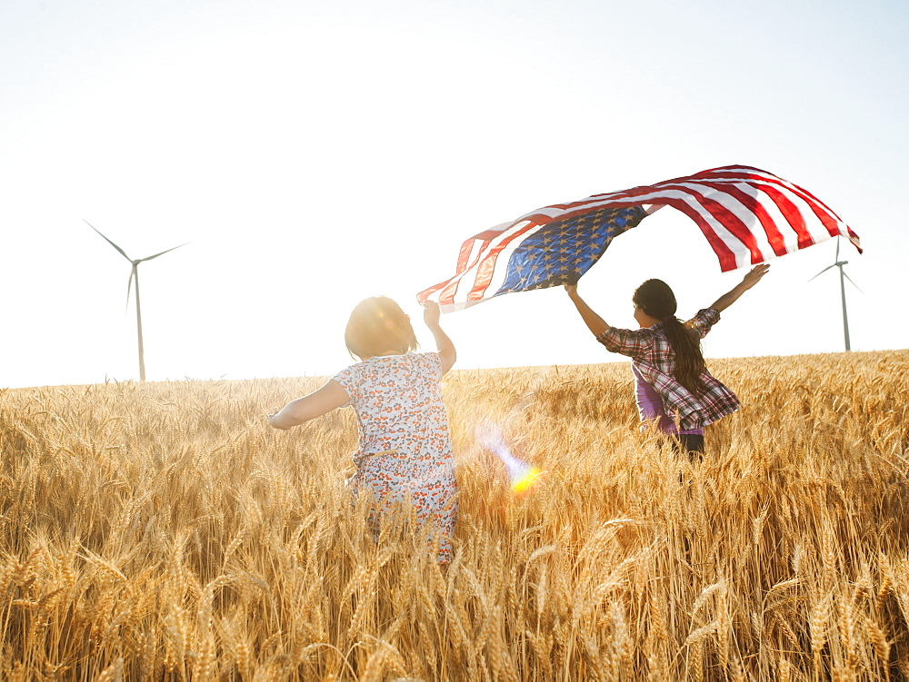 Girls (10-11, 12-13) flying american flag in wheat field