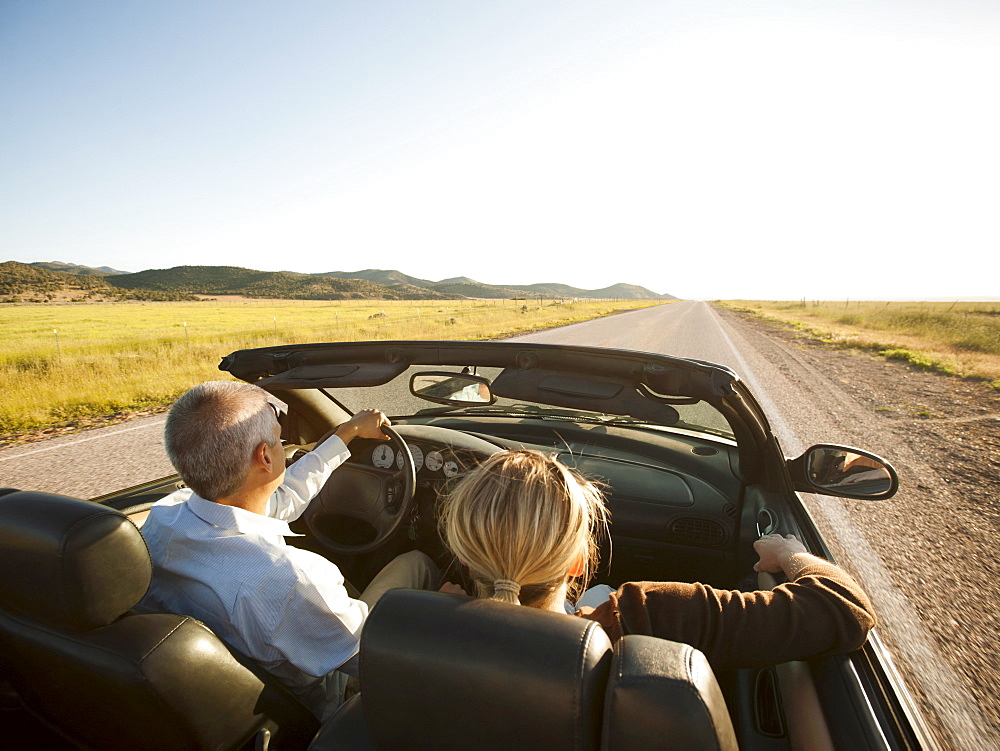 USA, Utah, Kanosh, Mad-adult couple driving through desert plains in convertible car