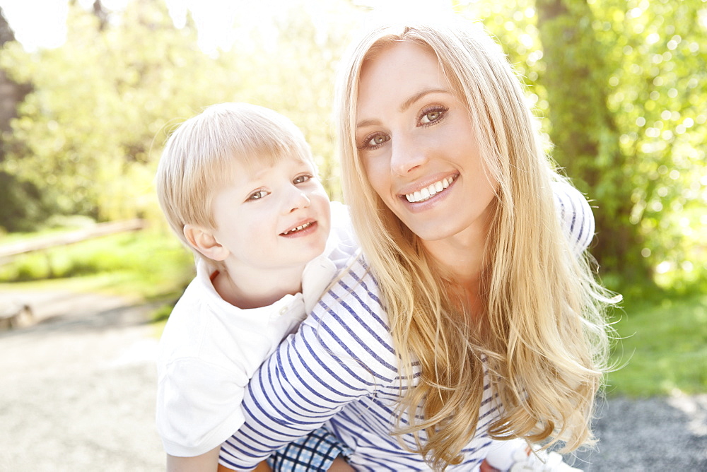 Young woman giving piggyback ride to son (2-3) in park