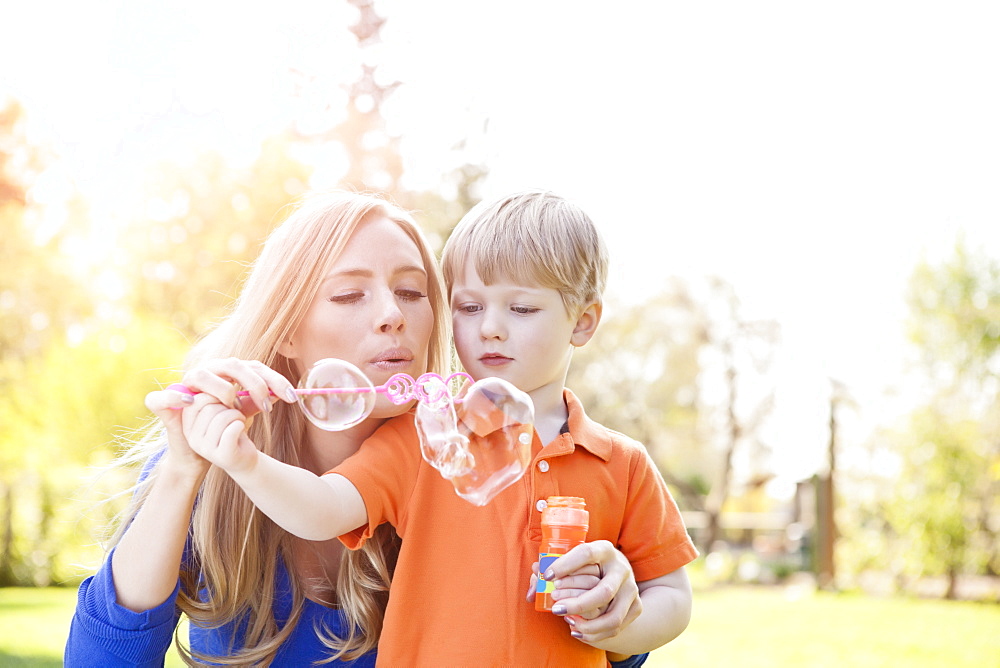 Mother and son (2-3) blowing bubbles in park