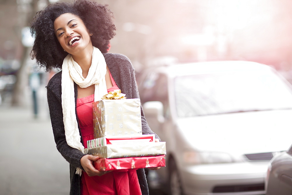 USA, Washington State, Seattle, Young cheerful woman carrying stack of boxed gifts