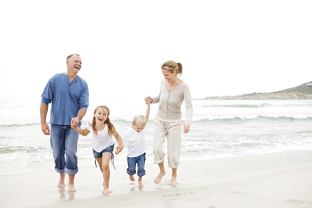 Smiling family holding hands and walking on beach