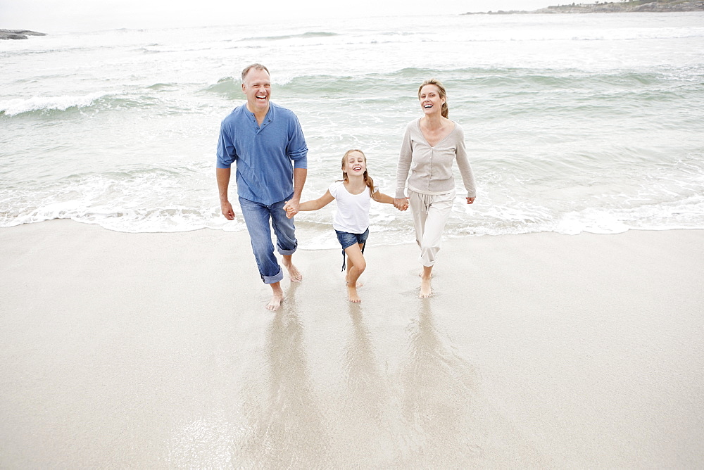 Smiling family holding hands and walking on beach