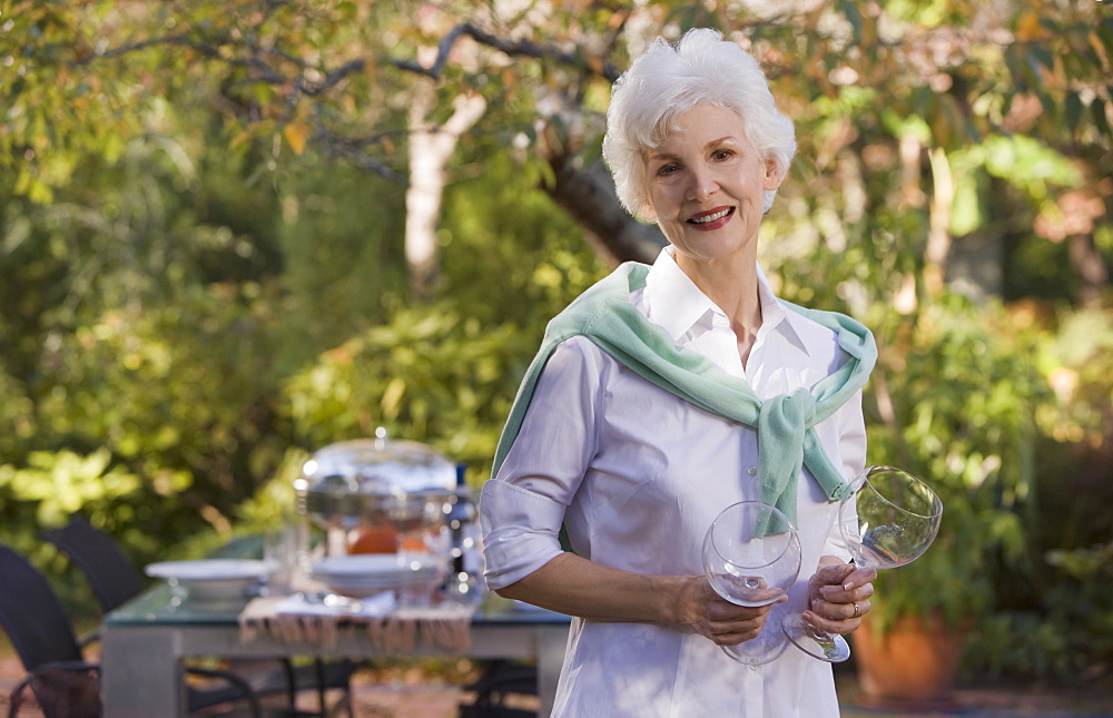 Senior woman standing in garden holding wineglasses