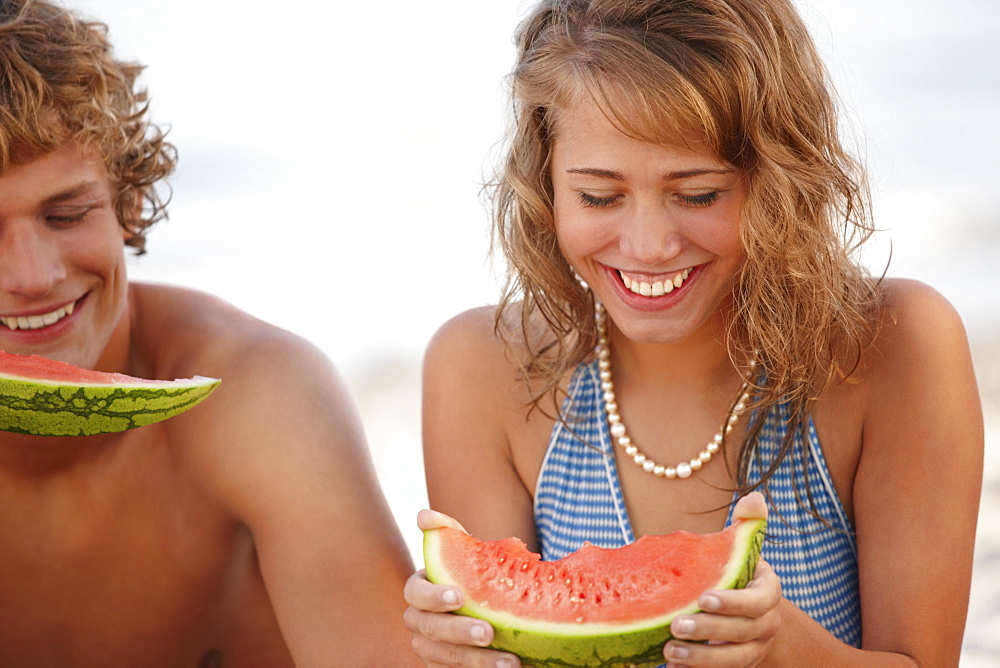 Young couple eating watermelon on beach