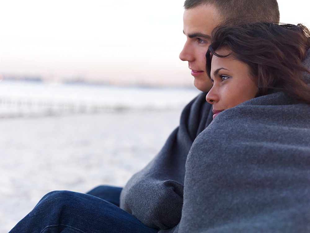 Young couple wrapped in blankets on beach