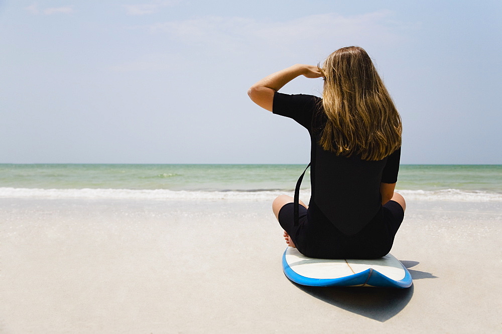 Girl sitting on surfboard, Florida, United States