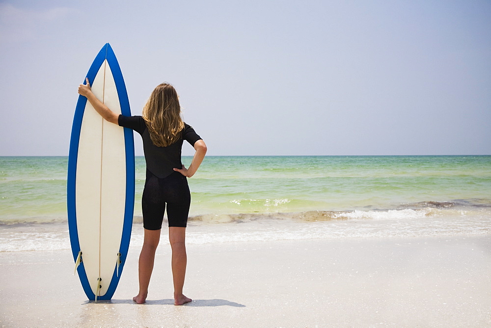 Girl holding surfboard in sand, Florida, United States