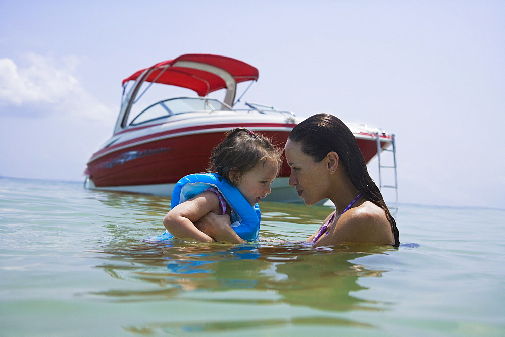 Mother helping daughter swim near boat, Florida, United States