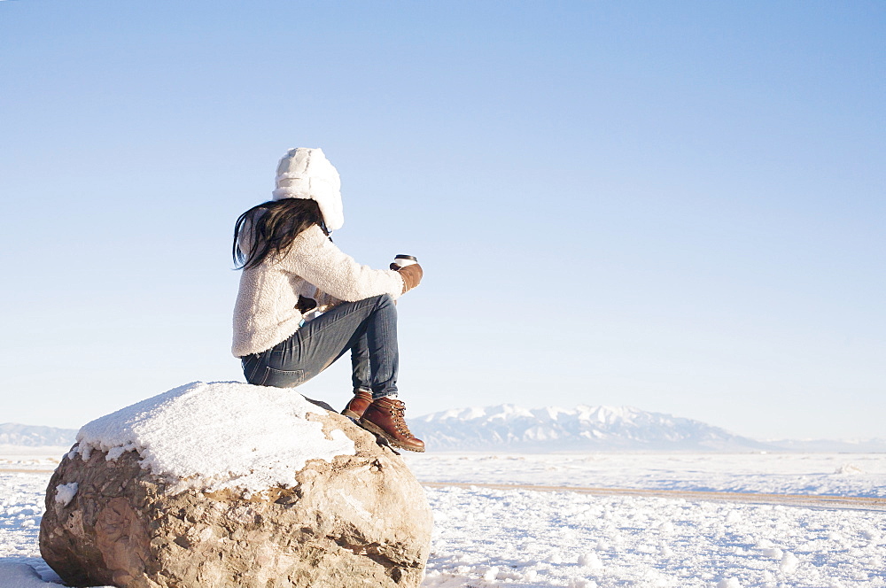 Woman sitting on rock with cup in winter, Colorado, USA