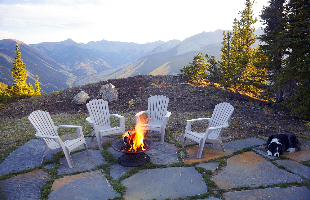 Dog lying down by fire pit and four empty chairs, Colorado, United States