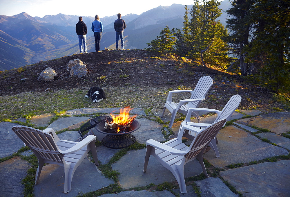 Three people standing near fire pit looking at landscape, Colorado, United States